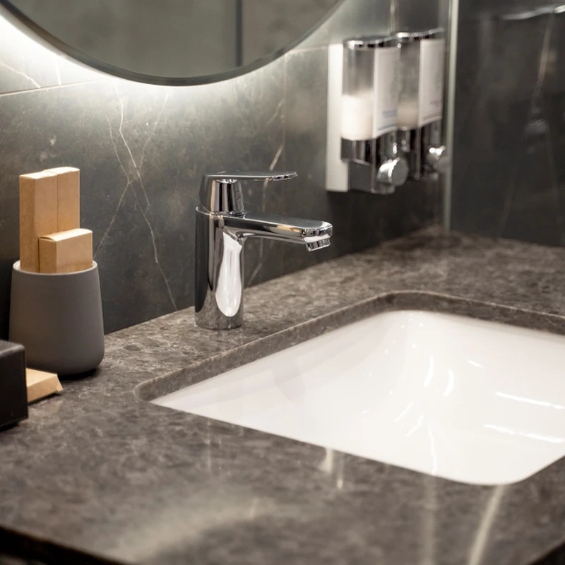 White ceramic basin and chrome mixer tap set into a dark grey marble-effect countertop in a bathroom.