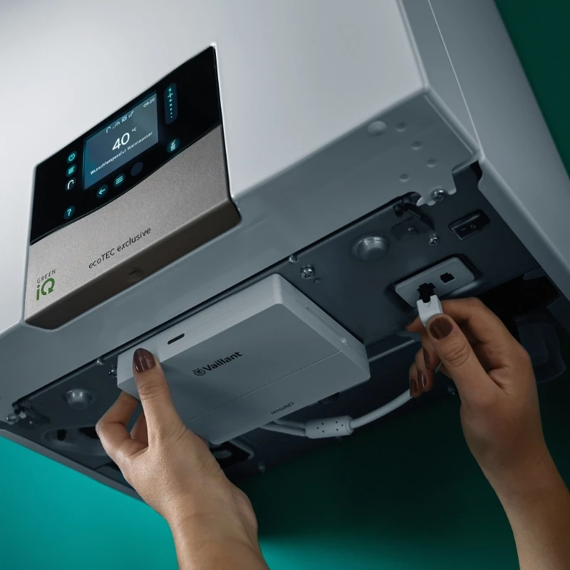 Hands installing a Vaillant VR900NET module and connecting a cable to a white ecoTEC exclusive boiler.