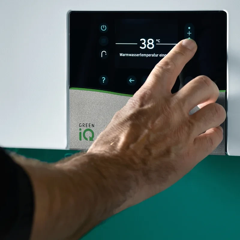 Hand increasing hot water temperature on a GREEN iQ digital boiler control panel, showing 38 °C.