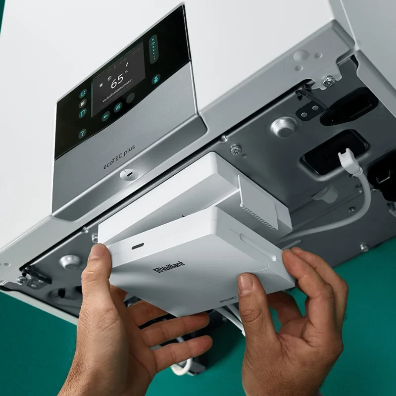 Hands inserting a Vaillant sensoNET module into a white Vaillant ecoTEC plus boiler.
