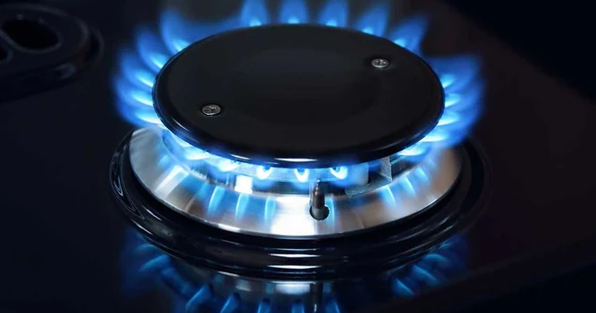 A gas hob burner with vivid blue flames on a dark, reflective kitchen surface.