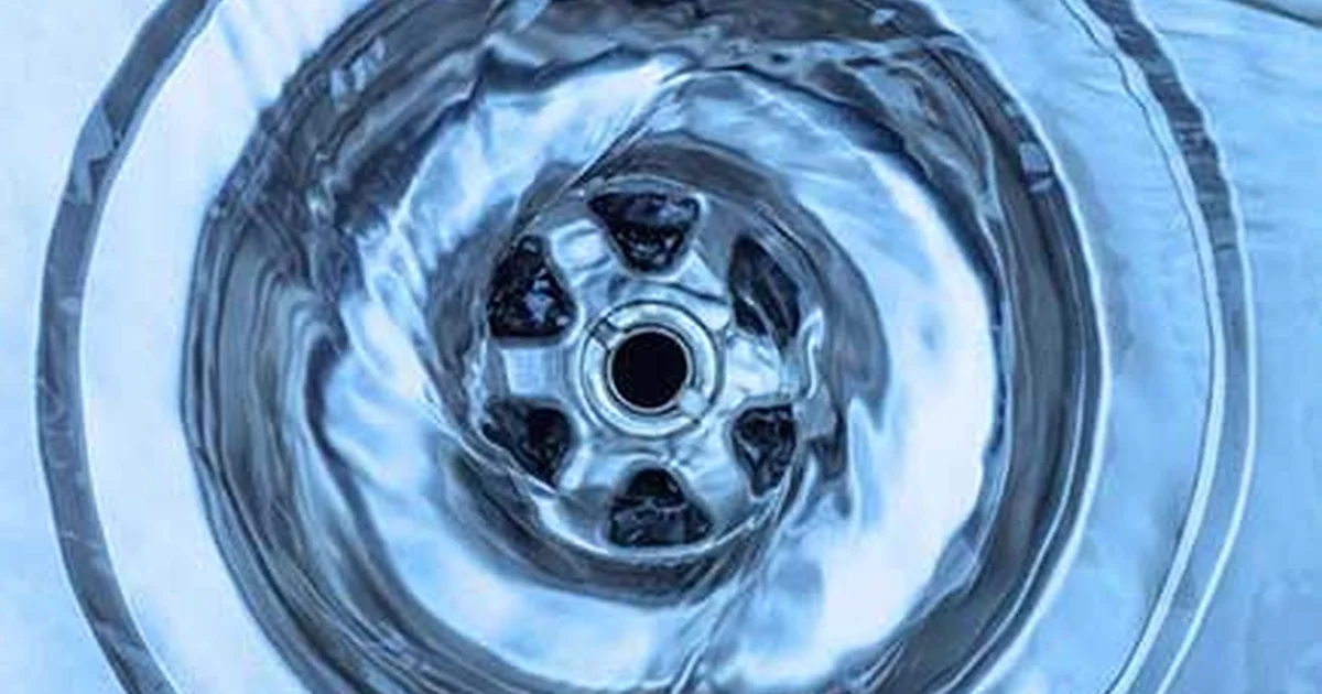 Clear water swirling powerfully down a metallic plughole in a light blue basin.
