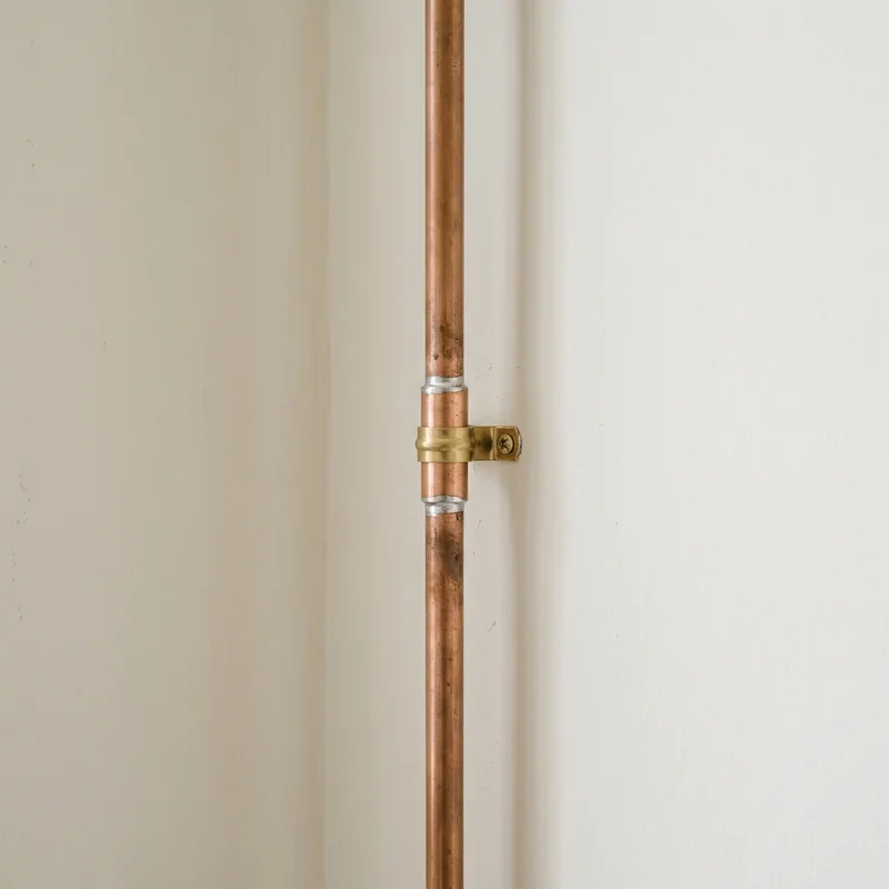 Vertical copper pipe with soldered joints, secured to a light-coloured wall by a brass pipe clip.