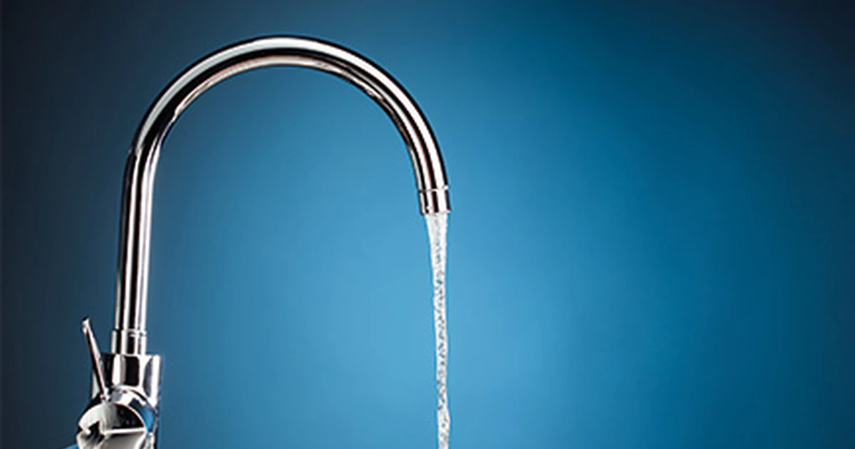 Water flowing from a polished chrome kitchen mixer tap against a deep blue background.